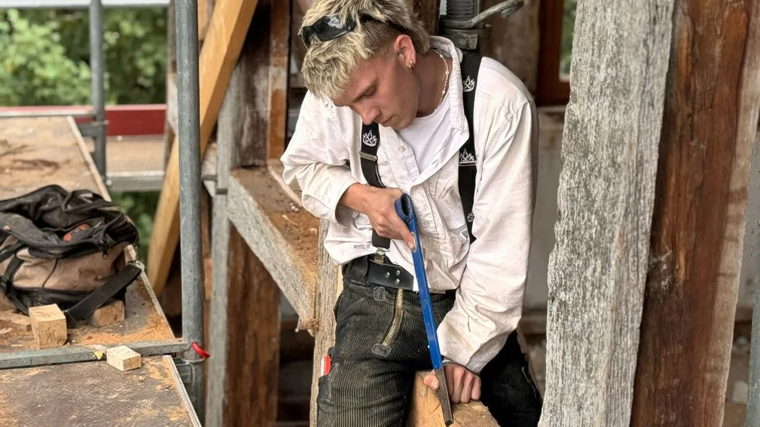 Auch der Auszubildende Leonhard packt kräftig mit an: Auf einem Balken sitzend macht er mit der Stoßaxt die Feinarbeit.